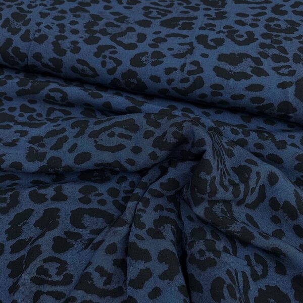 Tela de vestir de viscosa 100% estampado animal print de pantera con manchas en negro y fondo azul índigo.