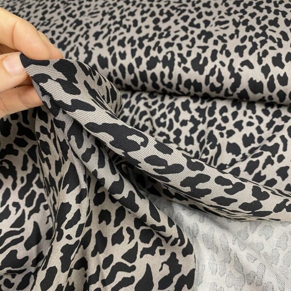 Tela de vestir de viscosa 100% tipo twill o sarga, con estampado animal print de leopardo con manchas en negro y fondo gris claro.