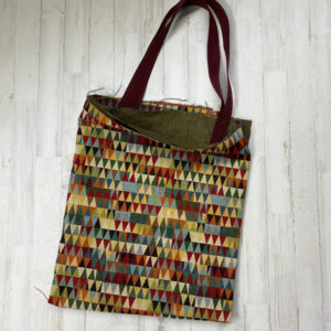 Pack Tote Bag con tela de gobelino estampado de cenefa de triángulos, interior jaspeado verde y cinta de espiga de 3 mm en color granate.