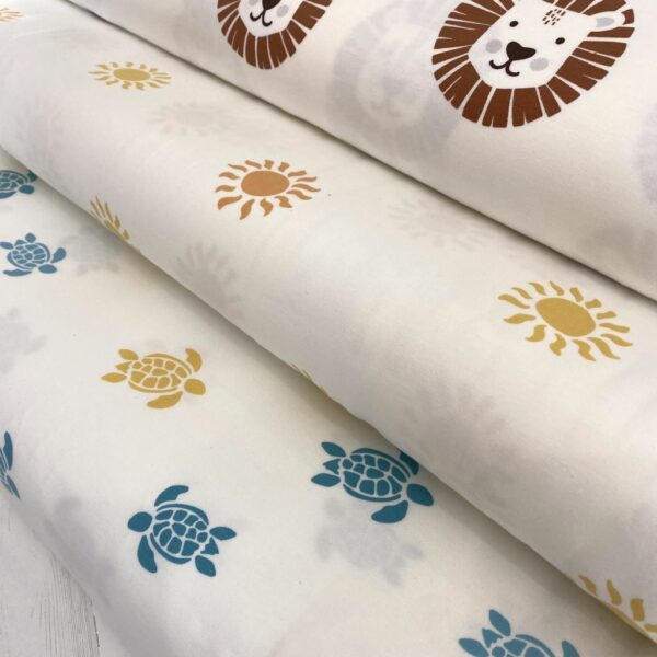 Tela de punto de camiseta de algodón orgánico. Tipo Jersey estampado con leones amarillos y marrones fondo blanco leones soles y tortugas
