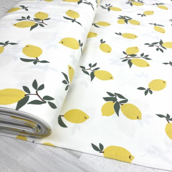 Tela de punto de camiseta de algodón orgánico. Tipo Jersey estampado con limones amarillos fondo blanco roto