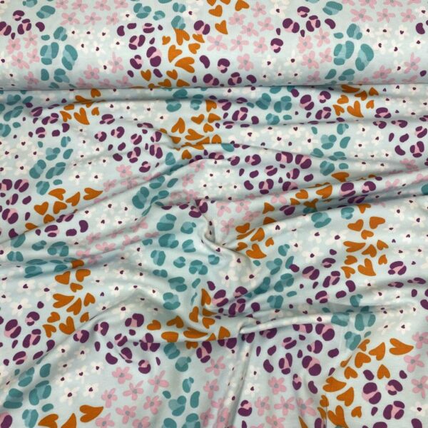 Tela de punto de camiseta de algodón orgánico. Tipo Jersey estampado con corazones en animal print fondo azul claro.