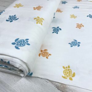 Tela de punto de camiseta de algodón orgánico. Tipo Jersey estampado con tortugas amarillas, naranjas y azules fondo blanco roto