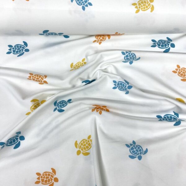 Tela de punto de camiseta de algodón orgánico. Tipo Jersey estampado con tortugas amarillas, naranjas y azules fondo blanco roto