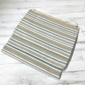 Retal de tela de tapicería gobelino estampado con cenefa en azul y ocre fondo crudo.