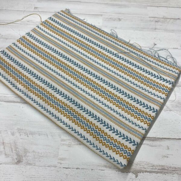 Retal de tela de tapicería gobelino estampado con cenefa en azul y ocre fondo crudo.